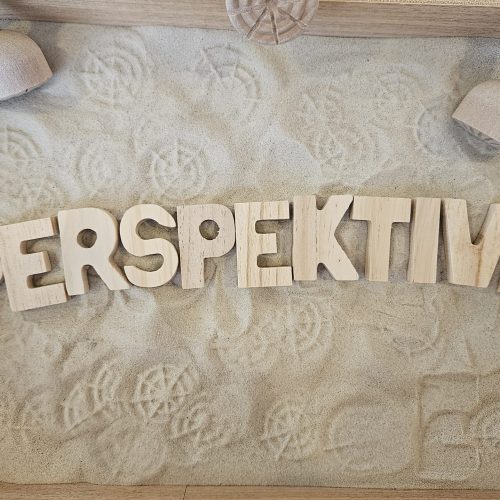 mit Holzbuchstaben steht in Sand geschrieben "Perspektive"